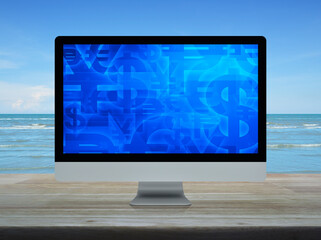 Financial currency symbol on desktop computer monitor screen on wooden table over tropical sea and blue sky with white clouds