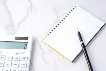電卓とペン、メモ帳でデスクワークをしているイメージ

