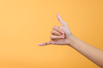 Woman hand showing calling hand gesture or shaka sign on yellow background