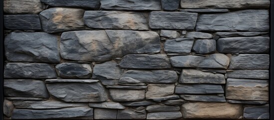 A detailed closeup of a grey stone wall with black brickwork framing, showcasing the intricate pattern of cobblestone building material used in the construction