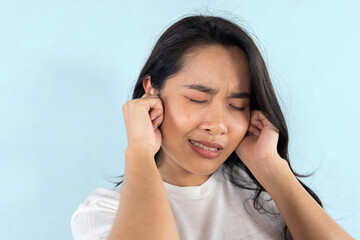 Young woman suffering from ear pain on light blue background.