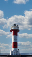 red lighthouse on a blue cloudy sky background. vertical orientation. - obrazy, fototapety, plakaty