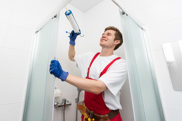 Naklejka na ściany i meble Young man repairing door of shower cabin in bathroom.