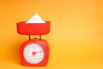 Plain flour on red plastic weighing scales over yellow background with copy space