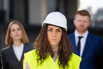 Portrait of serious woman construction architect with customer executives behind. Woman leadership...