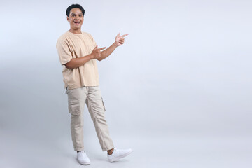 Stylish Asian man pointing with two finger aside to the empty space for ads or text with happy...