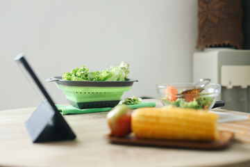 A lettuces in bowl on wooden table in the kitchens with tablet computer, corn and salad