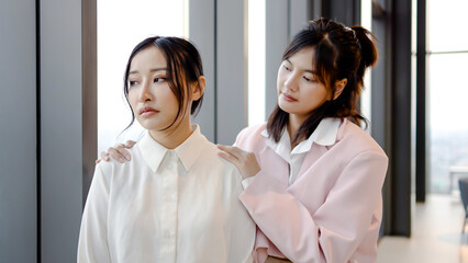 Young asian businesswoman calming down supporting sad friend standing near office. Portrait of young beautiful friends endorsing talking as lady waiting for smartphone message