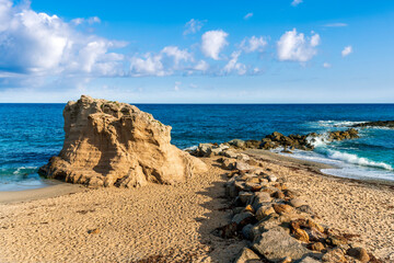 beautiful landscape of white sand beach with amazing waves during scenic sunrise or sunset with beautiful rock cliff , sea surf and nice cloudy sunset sky