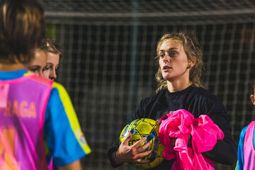 medium shot of a woman coach holding uniforms and a ball while talking to her soccer players. High...