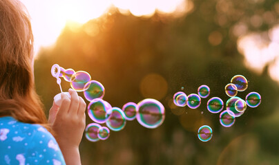 girl blowing soap bubbles outdoor, blurred natural sunny background. rear view. dreaming, harmony...
