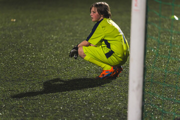 a young goalkeeper girl resting on the field i front of a goal-net, yellow uniform, school football team. High quality photo
