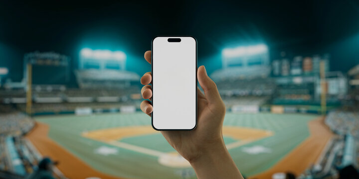 A hand holds a smartphone with a green screen at a baseball stadium