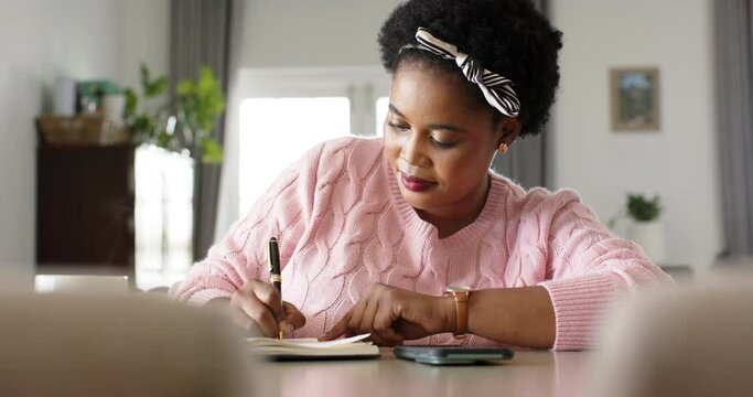 African American woman writes in a notebook at home