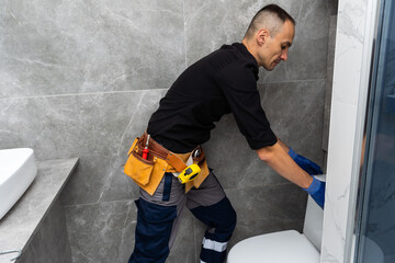 Professional plumber in uniform fixing toilet tank indoors