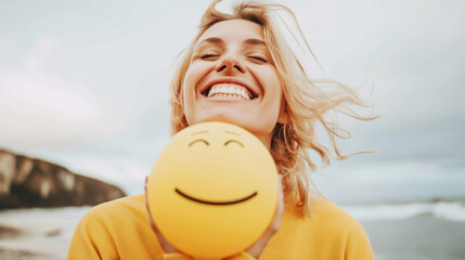 Happy young woman holding a yellow smiley on a beach