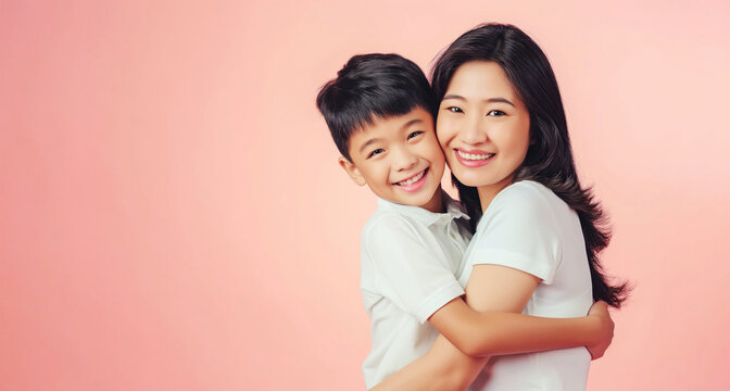 Young asian mother and son hugging and smiling in front of a pink background with copy space for Happy Mothers Day banner or flyer design