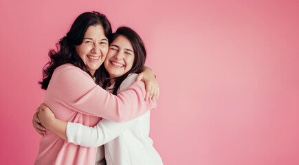 Happy Mothers Day banner background with a mom and her teenage daughter hugging and laughing in front of a pink background with copy space