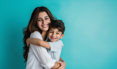 Middle eastern mother with her son hugging and smiling in front of a blue background with copy space for Happy Mothers Day banner or flyer template