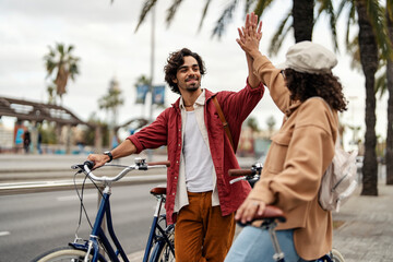Friends giving high five on the street while standing with their bicycles.