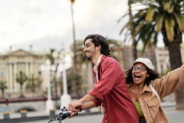 A happy trendy man is driving his girlfriend on bike on a street and having fun.