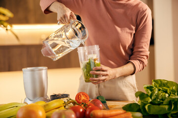 Cropped picture of a woman pouring water and preparing smoothie.
