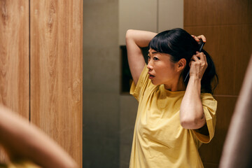 Reflection in a mirror of a japanese woman combing her hair in bathroom.