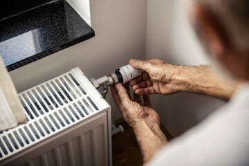 Close up of senior man's hands adjusting heating on valve.