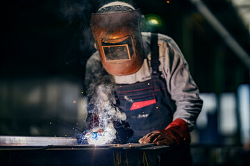 A heavy industry worker is welding at metallurgy factory.