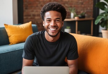 A smiling man in a black shirt uses a laptop in a contemporary living space with bright decor accents.