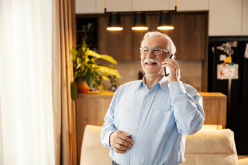 A senior man is talking on the phone at home.