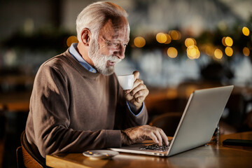 A senior entrepreneur sitting in coffee shop, coffee and working on a laptop.