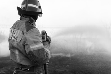 Fireman extinguishing a fire on a field. Black and white image.