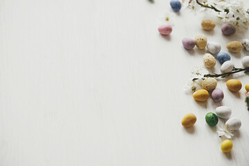 Happy Easter! Stylish easter chocolate eggs and cherry blossom on rustic white table flat lay. Easter border with space for text. Modern candy colorful eggs and spring flowers