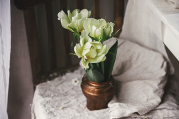 Stylish white tulips in vintage vase on old wooden chair with  linen cloth. Countryside rustic still life. Moody Spring flowers composition. Easter in country, floral banner