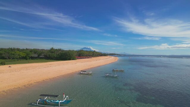 The camera flies over the first line of the coast with white sand and moored boats, a view of the volcano and mountains, a sandy beach selling a vacation plan from a copter, white sand and a mountain.
