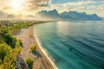 Naklejka premium Beautiful wide panorama of beach in Turkish resort Antalya. White line surf separates calm turquoise sea and Konyaalti beach with green parks and chain mountains in rays of evening sun at sunset