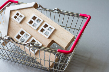 Miniature model of wooden house in shopping basket, concept of selling, buying or renting real estate