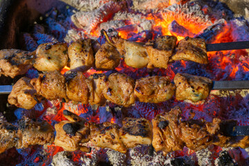 Fried pieces of meat strung on metal swords on coals. Drops of juice and fat are visible. High temperature coals