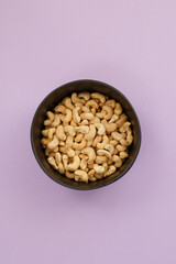 Cashew nuts in brown bowl on purple background close up.