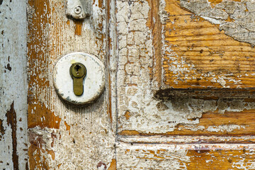 Old wooden door with cracked white paint. Brass lock embedded in the door. The wood texture is visible.