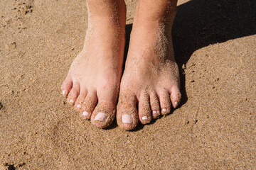 A person's feet are shown in the sand, with the toes sticking out