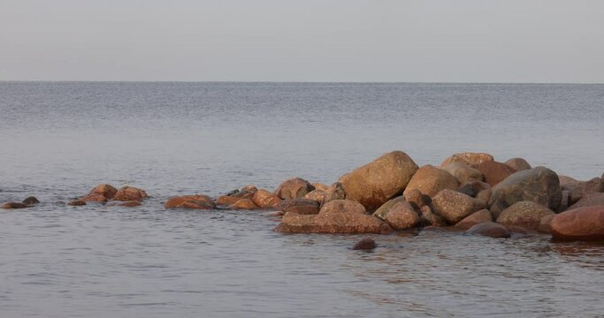 Calm blue sea and big rocks on the beach. The stones separate the photo and are in the center. The color is muted due to the fact that sunlight practically does not fall on them anymore, it is evening