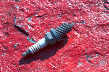 An old spark plug on a red stone surface background.