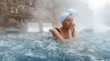 Young woman relaxing in outdoor hot thermal pool. Snowy winter day. Enjoying Spa