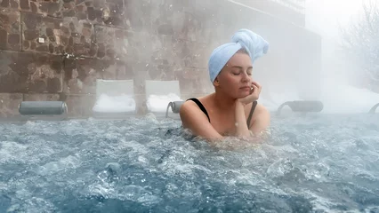 Gordijnen Young woman relaxing in outdoor hot thermal pool. Snowy winter day. Enjoying Spa © Terri_Crozier 