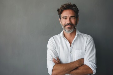A man with a white shirt and gray hair is standing in front of a gray wall