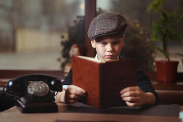 Engrossed young reader in cap with antique book and telephone