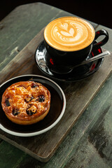 Cup of Cappuccino with beautiful cream latte art with a pastry on coffee shop table. Wooden background.