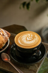 Cup of Cappuccino with beautiful cream latte art with a pastry on coffee shop table. Wooden background.